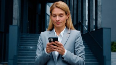 Genç bir kadın, elinde telefonuyla sosyal medyada iş e-postalarını yazarken gülümseyen iş kadınının akıllı telefondaki uzak internet iletişimi için cep telefonu uygulamasını kullanması mesajına cevap veriyor.