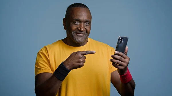 Mature man athlete instructor trainer watching sports training video on phone on internet sportsman looking for strength exercise in social network points to smartphone screen nods head in approval