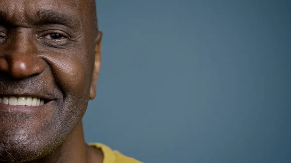 Close-up half male face with joyful expression mature african american man looking at camera smiling white healthy toothy smile happy customer satisfied with service posing in gray background studio