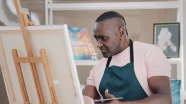 Afrika kökenli, yaşlı, 50 'li yaşlarda orta yaşlı, erkek bir ressam resim çiziyor. Resim dersinde resim çiziyor. Sanat eserlerinden esinlenerek yaratıcı fikirler anlatıyor.