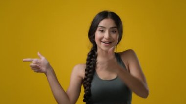 Stüdyo sarı arka plandaki kadın Hintli sporcu bayan dans eden atlet kız komik dans ediyor fotokopi reklamı için boş bir yeri işaret ediyor elleriyle teklif sunuyor.
