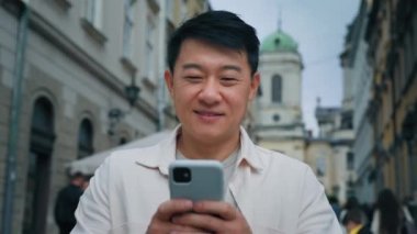 Arka planda duran mutlu erkek gezgin güzel şehir manzaralı turist elinde telefonla sosyal ağda iletişim kuruyor akıllı telefondaki konumlandırmayı cep telefonu uygulaması kullanarak kullanıyor.