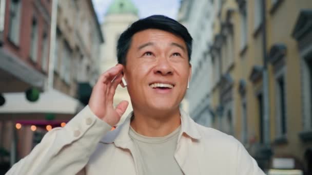 特写快乐快乐无忧无虑的搞笑男人在街上散步 用无线耳机听音乐 唱着快乐的中国男性游客喜欢在美丽的城市里散步 — 图库视频影像