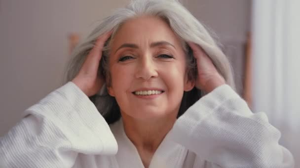 女性ポートレートクローズアップヘッドショット60歳中年シニア高齢者白人女性祖母シニア50代女性モデルとともに長いです光沢のある滑らかな灰色の髪笑顔見ますカメラ風ヘアケア — ストック動画
