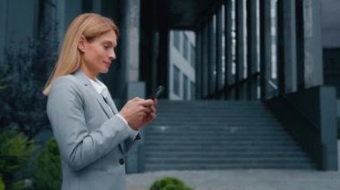 Odaklanmış başarılı iş kadını elinde akıllı telefonuyla geziyor sosyal medyada arkadaşlarıyla iletişim kurmak için e-posta yazıyor cep telefonu ile çevrimiçi mağaza penceresinde sipariş veriyor.