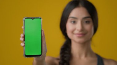 Sarı stüdyo arka planında Hintli etnik kadın bayan akıllı telefon cep telefonu ekranını yeşil boş krom tuşlu dokunmatik ekran teknoloji cep telefonu görüntüsü web servis reklamını gösteriyor