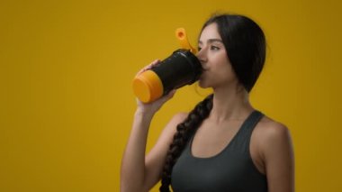 Stüdyoda sarı arka planda bayan sporcu bayan sporcu bayan milkshake 'den su içiyor sıvı kalsiyum vitaminler protein besin takviyeleri su dengesi kilo verme bakımı