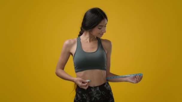 快乐苗条的女性在演播室黄色背景下印度女运动员女运动员用尺码测量腰围身材体形的测量带检查饮食健身运动减肥效果 — 图库视频影像