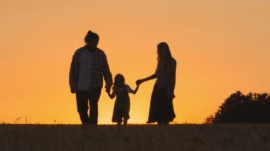 Aile siluetleri, sevgi dolu anne-baba, küçük kızı olan kadın, küçük kız çocuk, gün batımında buğday tarlasında yürüyor, atlıyor, gün batımında gün batımında dışarıda yürüyor, güneş batımında yürüyor.
