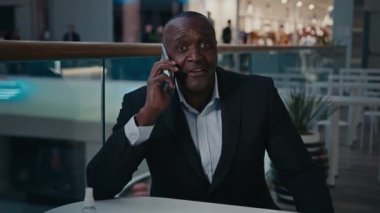 Afro-Amerikalı yetişkin orta yaşlı yetişkin bir adam ofis masasında çalışan bir işadamı telefonda konuşuyor cep telefonu konuşmaları gülümsüyor iş görüşmelerini akıllı telefon görüşmeleriyle konuşuyor.