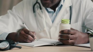 Bilinmeyen Afrikalı doktor kardiyolog eczacı, klinikte oturmuş, tıbbi tarif sağlık sigortası randevusu, bağışıklık için ilaç ve vitamin haplarının dozunu yazıyor.
