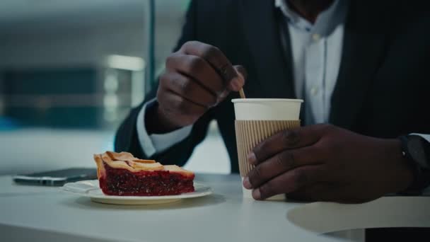 カフェのカフェテリアレストランでテーブルに座っている正式なスーツのアフリカ人男性労働者のビジネスマンは 芳香族コーヒーティーラテカプチーノドリンクのカップで砂糖を攪拌準備食べるチェリーケーキパイ — ストック動画