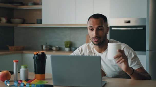 アフリカ系アメリカ人30代男性医師栄養士男性フィットネストレーナーは ラップトップコンピュータ上で瓶オンラインビデオ通話を示すスポーツダイエットビタミン食品サプリメントタンパク質を説明します患者ケア体重管理 — ストック動画