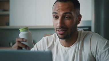 Afrikalı erkek beslenme uzmanı çevrimiçi fitness eğitmeni video konferansı mutfakta dizüstü bilgisayarla protein vitaminleri hakkında konuşuyor internet ticareti beslenme takviyeleri fitness kavanozu