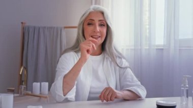 Yaşlı beyaz kadın, son sınıf güzeli, kamera güzellik blogu vlog konferansı ile konuşuyor. Kadın dokunuşu, buruşuk yüz makyajı yapıyor. Makyaj malzemesi, yüz kremi, nemlendirici prosedür.