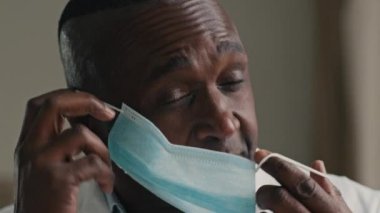 Deneyimli Afrikalı doktor etnik terapist kameraya bakıyor tıbbi maske takıyor ağız kapağını kapatıyor covid-19 Coronavirus salgınını önlemek için bireysel koruyucu solunum cihazı kullanıyor.