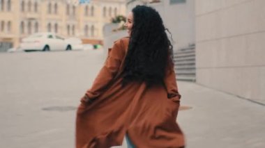 Mutlu aktif koşma tarzı Kafkasyalı kaygısız neşeli kız esmer 30 'lu yaşlardaki kadın şehirde dans ediyor sokak kadınlarının gülümsemesinden keyif alıyor.