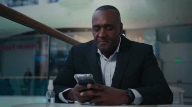 Afro-Amerikalı yetişkin yetişkin yetişkin yetişkin erkek çalışan işadamı ofis kafeteryasında, telefon kulübesinde sohbet ediyor cep telefonu sohbetleri yapıyor cep telefonu sohbetleri yapıyor akıllı telefonları karıştırıyor.