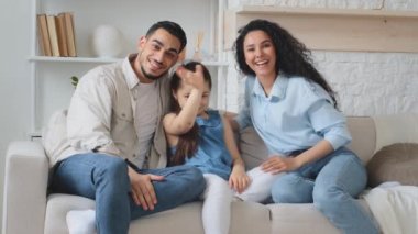 Çok ırklı, etnik çeşitliliğe sahip İspanyol kökenli Arap bir aile, Hintli bir ebeveyn, kızı olan bir anne, kanepede oturmuş el sallıyor ve internette sohbet konferansında konuşuyor.