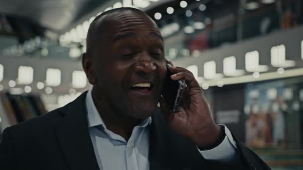 ハッピー陽気な優しい話アフリカの中年男性大人50ビジネスマン男性屋内で会社モールショッピングセンター答えコールトーク携帯電話の会話は笑顔スマートフォンを話す笑顔 — ストック動画