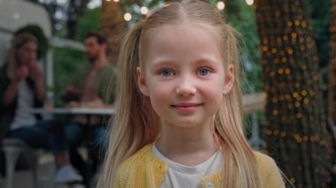 Dışarıdaki küçük şirin çocuk portresini kapat kamp yapan küçük kız bebek okul kızı kameraya bak beyaz anne ve baba kamp alanında yemek yiyor anne ve baba arka planda konuşuyor.