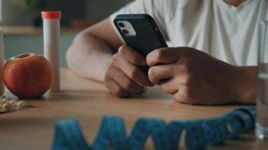 Erkek ellerini kapat cep telefonlu adam beslenme uzmanı tanınmayan erkek spor eğitmeni akıllı telefon uygulamalı kalori sayıyor sağlıklı beslenme fitness diyeti elma vitamini hapları mezurası ile