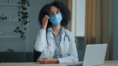 Kadın doktor yoğun iş gününü hastanede tamamlar. Coronavirus salgınından sonra tıbbi maske solunum cihazını çıkartır. Derin nefes alma temiz hava eksikliğini azaltır. Etnik Afrikalı kadın stajyer covid-19 salgınında çalışıyor.