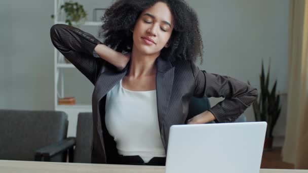 疲れアフリカの女性のビジネス女性の従業員は オフィスの机に座っているコンピュータの仕事の後に戻って筋肉の緊張疲労を感じるマッサージ首は健康な体の体操のリラクゼーションを行う背骨のけいれんを緩和します — ストック動画