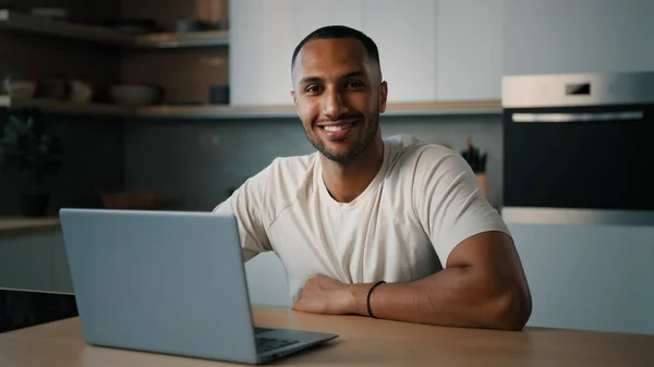 Smiling African millennial man guy American male user freelancer at home kitchen finish distant work with laptop satisfied with computer app online website networking shopping looking at camera smile