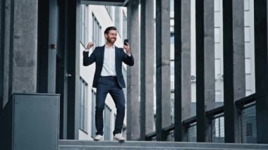 Hevesli adam ofis binasının yanında duruyor. Cep telefonundan iyi haberler okuyor. Heyecanlı iş adamı başarıyı kutluyor.