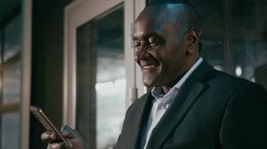 Mutlu gülümseyen olgun bir adam, elinde telefonuyla e-posta yazarken cep telefonu kullanıyor. Uygulamalı iş adamı, müşterisiyle internet üzerinden iletişim kuruyor ve akıllı telefon kullanıyor.