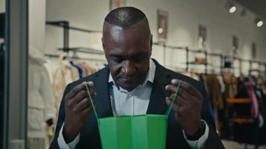 Afro-Amerikalı yetişkin orta yaşlı iş adamı alışveriş merkezinde alışveriş torbası satın alan erkek tüketici kötü tepkilerden memnun kalmayan mevcut alımlarla üzgün bir başarısızlık yaşıyor.