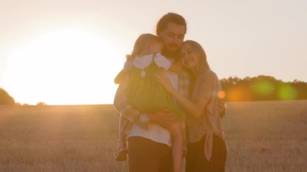 家庭假日周末在公园的室外 夕阳西下阳光普照的三个轮廓可爱的父母和女儿拥抱在麦田里拥抱拥抱的小女孩 — 图库视频影像