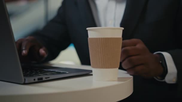 カフェテリアのテーブルにノートパソコンを入力して男性の手を閉じます Cropped Viewアフリカの成人中高年実業家男性労働者起業家オンラインで働いている雇用主の男性カフェでコーヒーを飲むコンピュータ — ストック動画
