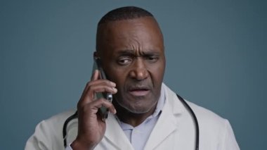 Olgun ciddi bir doktor, hasta memnuniyetsiz bir adamla telefonda konuşuyor. Stüdyoda gri arka planda duruyor. Uzaktan kumandalı telefon reddi anlaşmazlığı ile iletişim kuruyor.
