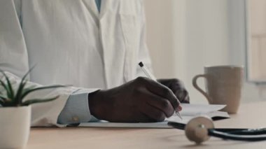 Tanımlanamayan erkek doktor kardiyolog, doktor ceketi giyer. Masaya oturur, defter planlama çalışmalarına teşhis yazar. İlaç sonuçları yazar, profesyonel tavsiyeler yazar.