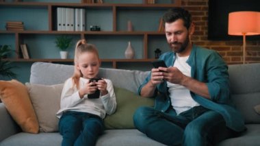 Kafkasyalı bekar baba ve çocuk anaokulu öğrencisi kız kanepede oturup cep telefonu sohbetlerine bakıyorlar. Ev Wi-Fi akıllı telefon uygulamaları kullanıyorlar. Genç aile internet bağımlıları modern aletler teknolojileri aşırı kullanıyorlar.
