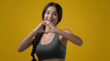 Hint etnik kadın bayan bayan sporcu spor kızı spor spor spor eğitmeni sarı stüdyo arka planında kalp şeklini gösteren sevgi dolu sevgi dolu umut dolu romantik bir jest.