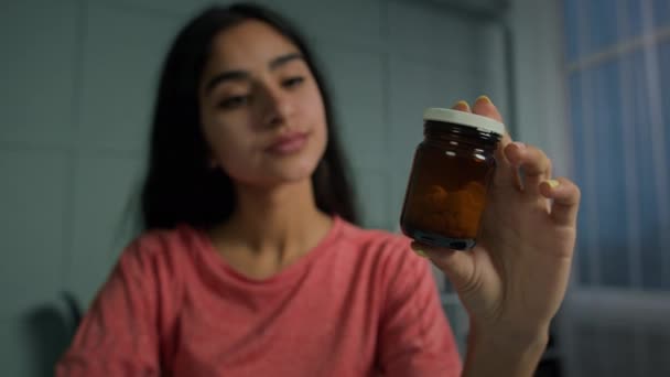 年轻的阿拉伯西班牙女人拿着装有药丸的瓶子读着药方 女性病人吃药准备喝止痛药片 用于流产或健康免疫 — 图库视频影像
