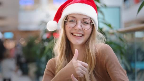 閉じるアップ幸せな白人女性で赤サンタクリスマス帽子キャップと眼鏡陽気な女の子女性ショー親指アップ屋内同意勧告手ジェスチャーダンスとともに腕成功新年楽しい勝利 — ストック動画