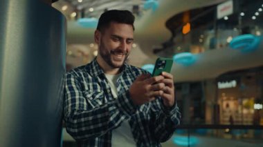 Genç adam blogcu Arap İspanyol işadamı alışveriş merkezinde duruyor. Mobil ekran mesajlaşması e-postasına bakıyor. Cep telefonundan internet üzerinden ürün satın alma konusunda olumlu haberler okuyor.