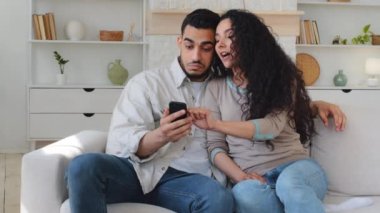 Duygusal tartışmalarda evli karı koca, İspanyol erkek ve Kafkasyalı kadın telefon gezintisi uygulaması kullanarak kanepede oturuyor ve internetten yemek siparişi veriyor.
