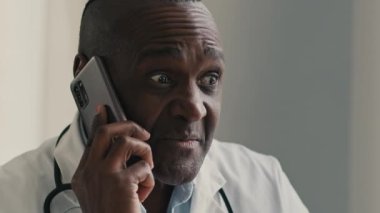 Afrikalı Amerikalı etnik doktor erkek terapist. Cep telefonuyla hastaya danışmanlık yapıyor. Erkek profesyonel danışman.