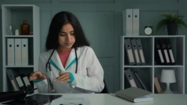 Genç doktor, masa başı planlama günü oturup evraklarla çalışıyor. Tıp sigortası belgeleri yazıyor. Arap kadın pratisyen doktor sağlık geçmişi formlarını dolduruyor.