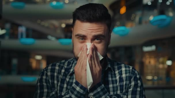 ショッピングセンターで病気のアラビア人男性若い男性アレルギー男は鼻水インフルエンザ疾患に苦しんでいます季節のアレルギーカバー口のくしゃみ紙ナプキンで鼻を拭くウイルス症状コロナウイルス感染症を持っています — ストック動画