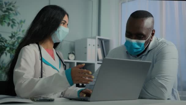病院での女性医師とアフリカの高齢者の患者は ラップトップを使用して座ってアラビア語の医師は コンピュータ上の電子断層撮影の結果オンライン健康診断医療処方を説明します近代的な技術相談 — ストック動画