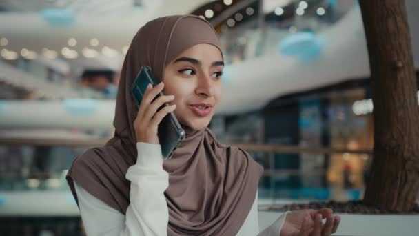 美しいですイスラム教徒女性でヒジャーブ公共の場所に座っている話携帯電話でショッピングモール女性千年紀アラビア語女の子リラックスビジネス女性呼び出し遠くに友人議論ビジネス会話 — ストック動画