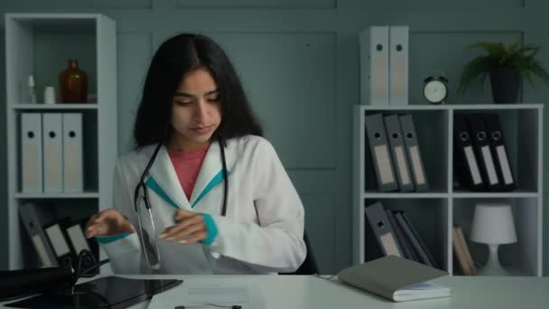 女性の若い医師は 文書で作業机の計画日に座っている医療保険アラビア語の女性の一般開業医は ジャーナルで健康履歴書を記入書き込みジョブレポートを作る — ストック動画