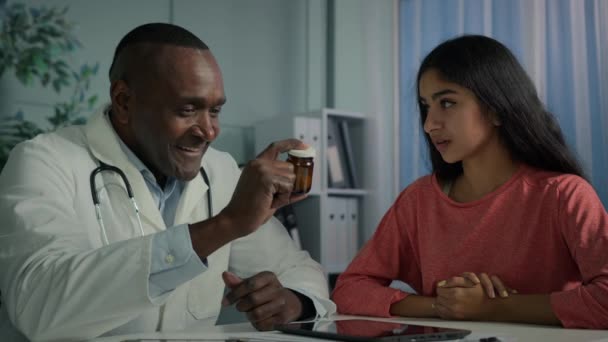 アフリカの男性セラピスト医師一般開業医は 患者が抗うつ薬のホルモンビタミン薬で医療用ボトルを与える相談してください 病気アラビア人女性もらいますプロフェッショナル支援で病院 — ストック動画
