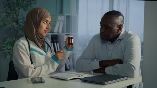 イスラム教徒のアラビア語中東女性医師セラピスト薬剤師不健康な患者に話すアフリカ人男性は薬の丸薬とボトルを与える高齢者世代のための薬物投与の専門薬を説明します — ストック動画